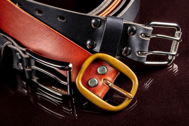 Plusieurs ceintures en cuir avec une boucle en métal sur fond sombre