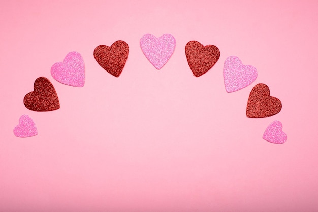 Plusieurs coeurs avec des paillettes formant un arc sur fond rose Concept d'amour
