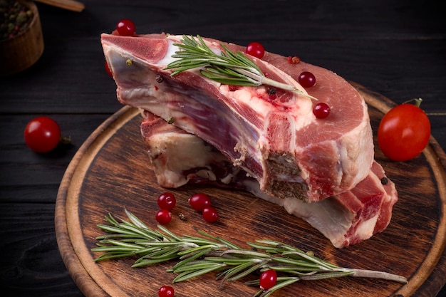 Plusieurs morceaux de poitrine de boeuf crue sur l'os avec des canneberges, du romarin et des tomates cerises sur un fond en bois sombre.