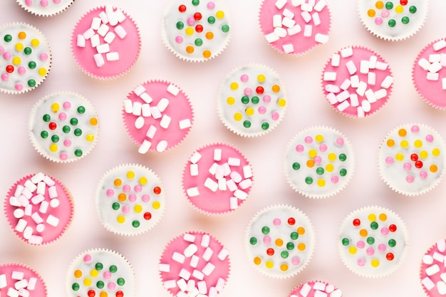 Plusieurs muffins colorés joliment décorés sur fond blanc, vue du dessus.