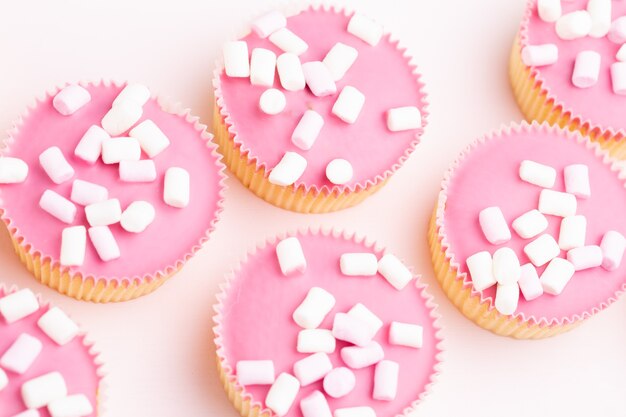 Plusieurs muffins colorés joliment décorés sur une surface rose, vue du dessus.