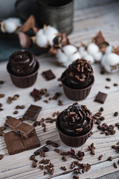 Plusieurs Muffins Ou Cupcakes à La Crème En Forme De Chocolat à Table Blanche. Bougie Festive Brûle Sur Un Gâteau Au Chocolat. Il Y A Des Pépites De Chocolat Dispersées à Proximité