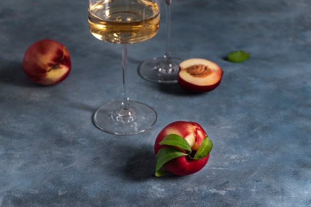 Plusieurs pêches ou nectarines mûres et un verre de vin de pêche blanc