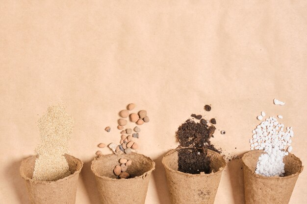 Plusieurs pots de tourbe avec différents ingrédients pour préparer un sol fertile pour les plantes, des pierres pour le drainage, de la perlite, de la terre pour les semis, de l'engrais pour le jardin