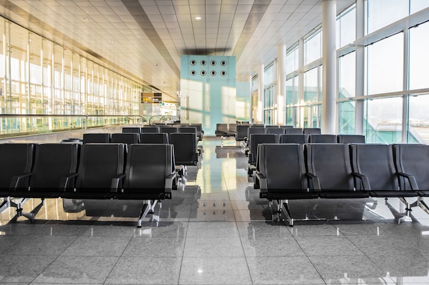 Plusieurs rangées de sièges noirs modernes dans la salle d'attente ensoleillée vide de l'aéroport