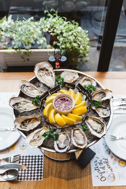 Plusieurs sortes d&#39;huîtres fraîches servies dans un plateau rond avec une tranche de citron et une sauce épicée.