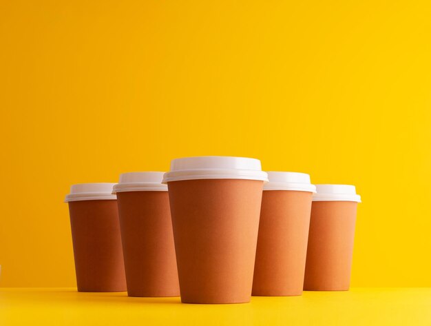 Plusieurs tasses à café jetables organisées en rangée sur fond jaune