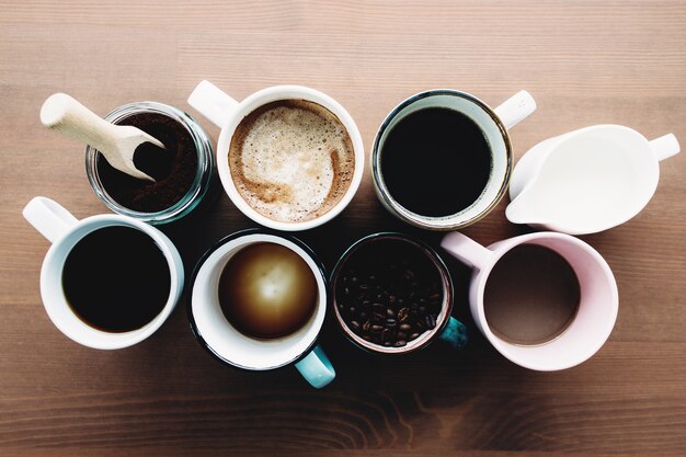 Plusieurs tasses à café, lait, haricots et café moulu en pot sur table en bois. Photo de haute qualité