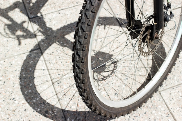 Pneu de roue avant de vélo et silhouette d'ombre sur la surface des carreaux de béton urbain