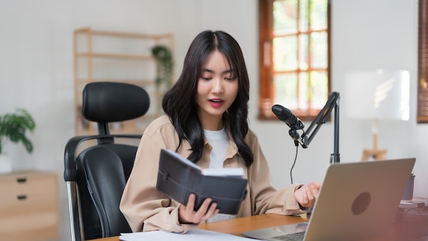 Podcasteur féminin lisant des notes de script pour parler du contenu tout en enregistrant un podcast audio en studio