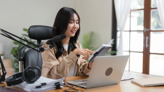 Podcasteur féminin lisant un scénario dans un bloc-notes et parlant du contenu pour faire un podcast audio en studio