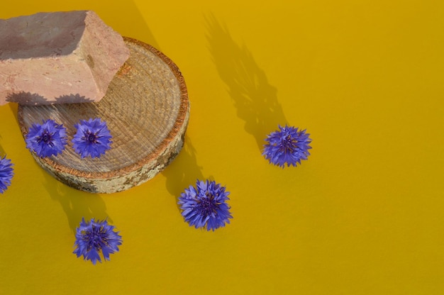 Un podium en bois avec des bleuets bleus sur fond jaune pour la présentation de produits naturels