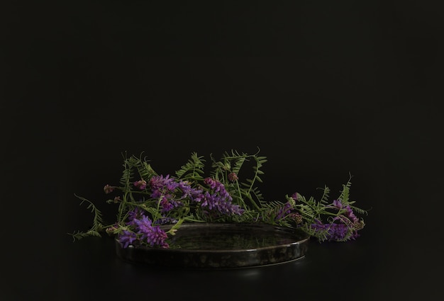 Podium noir sur fond noir avec des fleurs Podium pour la présentation cosmétique du produit