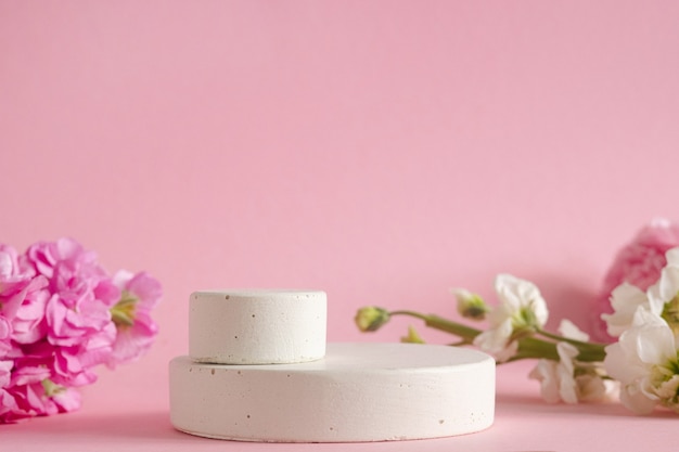 Podium vide pour la présentation des produits cosmétiques. Fleurs pastel sur fond rose vue latérale