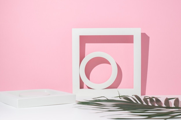 Podiums géométriques blancs pour présentation et feuille de palmier sur fond rose blanc.