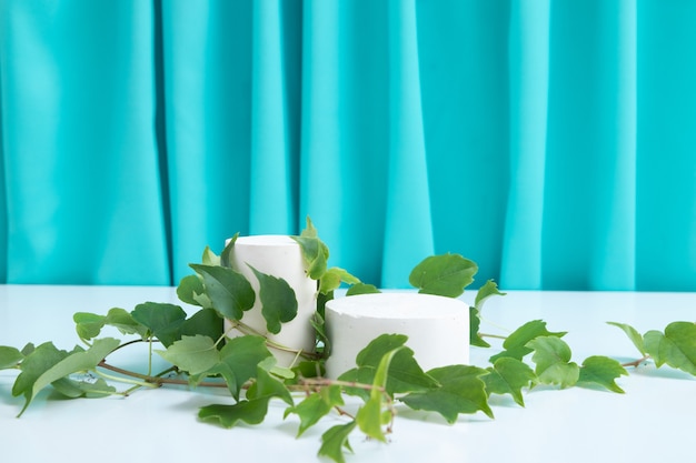 Podiums ou piédestal Maquette avec feuilles pour la production cosmétique sur fond turquoise avec plis de tissu.