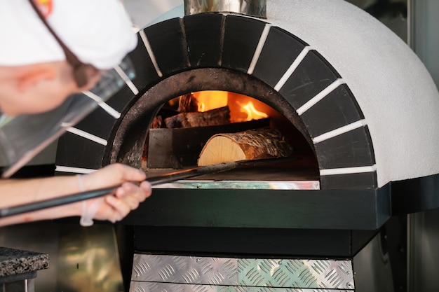 Poêle à bois à pizza italienne Le cuisinier ajoute du bois de chauffage au poêle