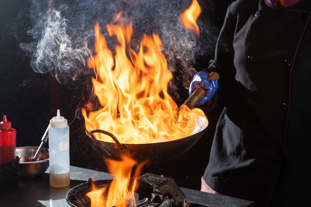 Poêle flambée wok, cuisson au feu. Cuisine pan-asiatique. L'alimentation de rue.