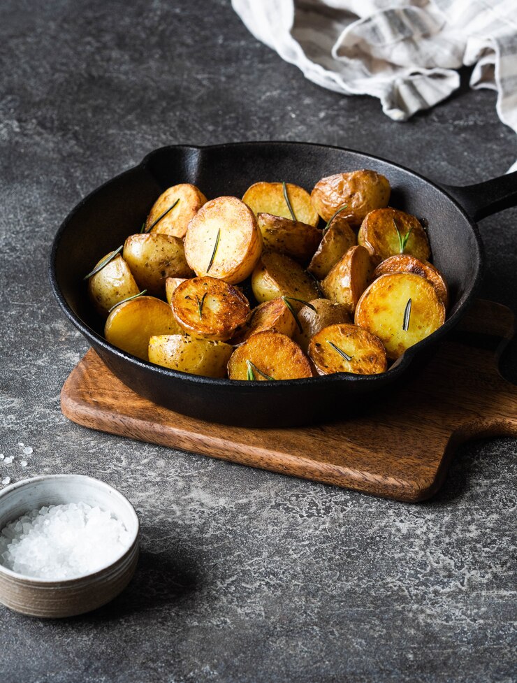 Poêle en fonte noire avec des quartiers de pommes de terre rôties frites aux herbes sur une surface gris foncé