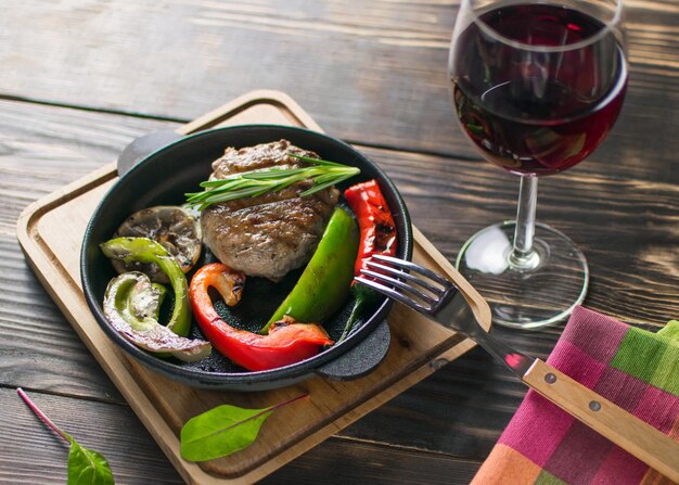 Poêle à frire avec une boulette de viande et des légumes et un verre de vin