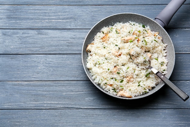 Poêle à frire avec de délicieux riz et poulet sur table en bois