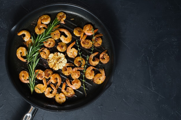 Poêle à frire avec des gambas frites et des brins de romarin et de thym.