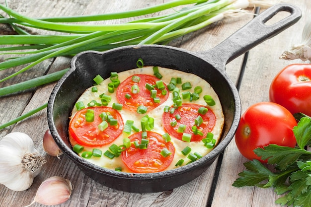 Poêle à frire noire avec des œufs brouillés et des tomates sur une table rustique en bois