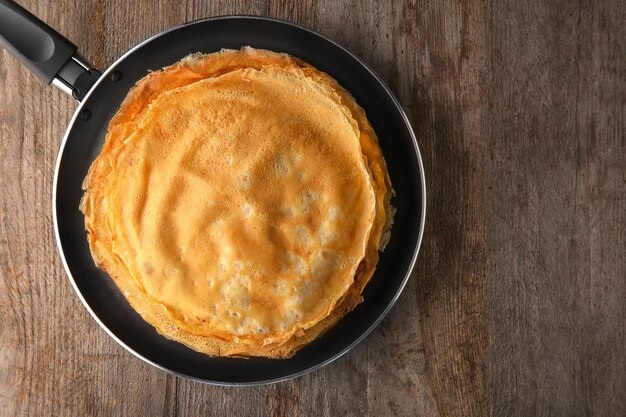 Poêle à frire avec pile de délicieuses crêpes minces sur table en bois