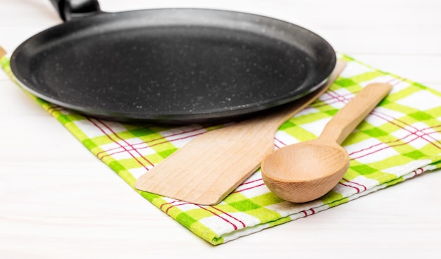 Poêle à frire avec ustensile en bois et torchon sur la table en bois blanc