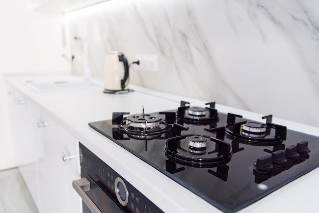 Photo poêle à gaz moderne de haute technologie noire avec panneau de capteur à l'intérieur lumineux de la cuisine avec des carreaux de marbre blanc.