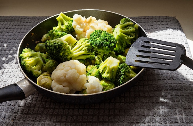 La poêle avec des légumes frais décongelés et une spatule de cuisine