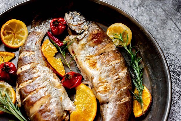 Une poêle de poisson avec des oranges et du romarin sur le côté