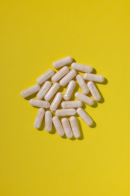 Une poignée de capsules blanches de vitamines et de suppléments alimentaires sur un fond jaune vif