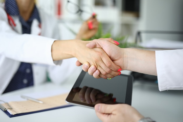 Poignée de main de deux médecins, l'un tient la tablette. Concept d'accords d'assurance médicale