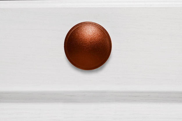 Poignée de meuble ronde de couleur bronze sur fond de bois blanc