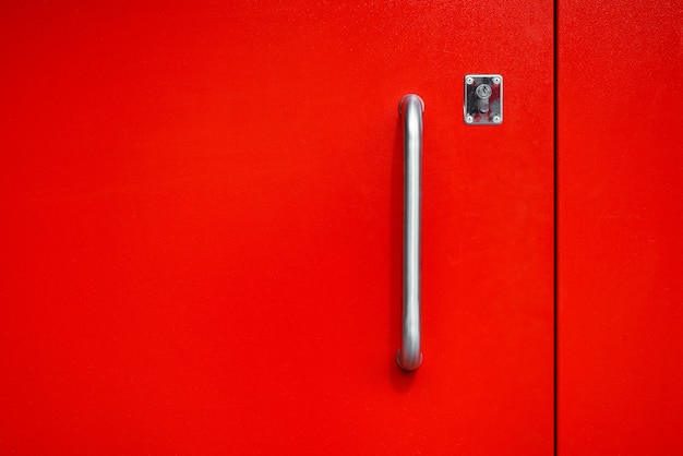 Poignée de porte en acier avec serrure et porte d'entrée en métal rouge vif, à l'extérieur. Texture en métal peint. Minimalisme