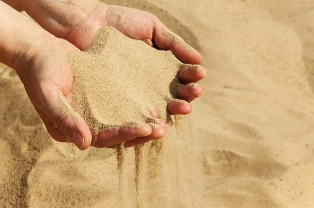 Poignée de sable dans les mains des femmes, mise au point sélective. Le sable coulant des mains féminines.