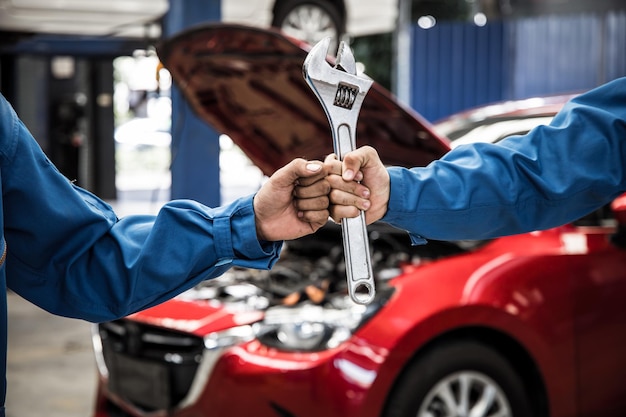 Photo poing et main de mécanicien avec l'outil de deux mécaniciens automobiles faisant l'entretien et la maintenance de la voiture. concept de service de réparation. réparation et entretien de voitures. mécanicien automobile travaillant au centre de service automobile.