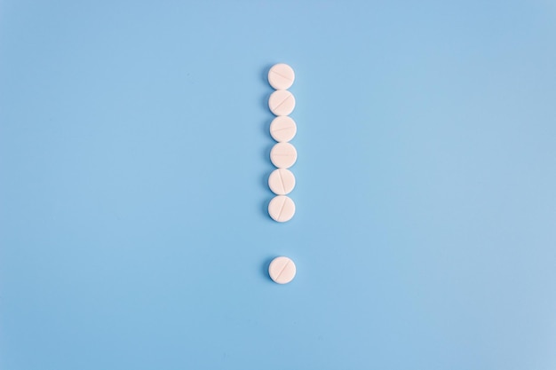 Point d'exclamation de pilules médicales sur fond bleu. Concept de thème de traitement.