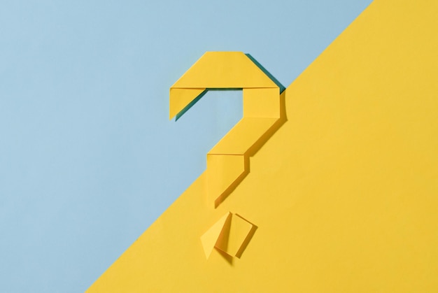 Point d'interrogation origami jaune sur un fond diagonal à deux tons de jaune et de bleu assortis placé au centre avec espace de copie