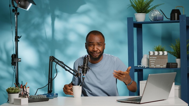 Point de vue d'un influenceur enregistrant un vlog et parlant aux abonnés devant la caméra. Vlogger utilisant un microphone et un ordinateur portable pour filmer une vidéo pour une chaîne de podcast sur les réseaux sociaux. Homme créant du contenu