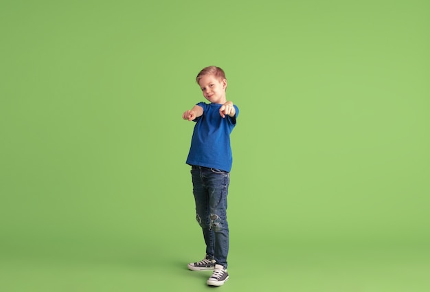 Pointant dessus. Heureux garçon jouant et s'amusant sur le mur vert. Un enfant de race blanche en tissu brillant a l'air enjoué, riant, souriant. Concept d'éducation, d'enfance, d'émotions, d'expression faciale.
