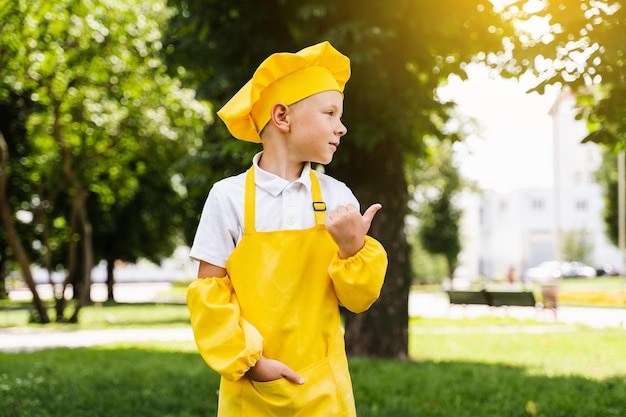 Pointez vers la droite Beau cuisinier enfant en chapeau de chef jaune et tablier jaune uniforme pointant vers la droite Publicité créative pour un magasin d'alimentation et un café