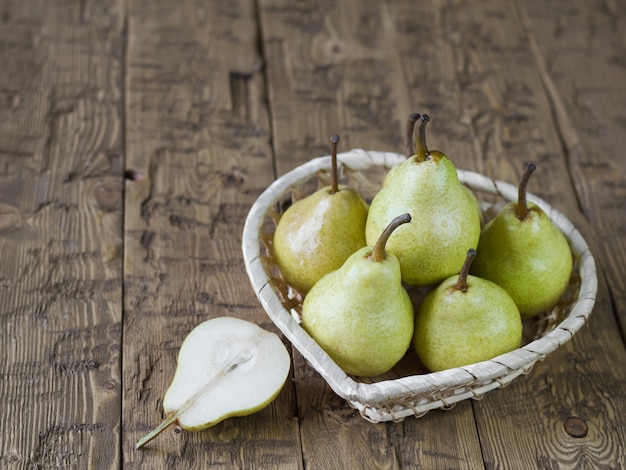 Une poire coupée et un panier avec des poires sur une table en bois.