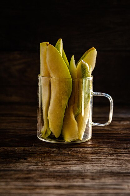 Poire en tranches dans une tasse en verre sur une table en bois de cuisine.