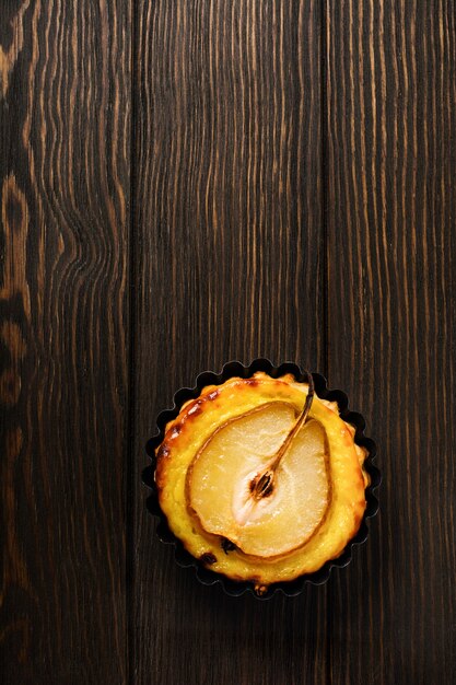 Poires et mini tartelettes à la crème sur une vieille table en bois brun foncé