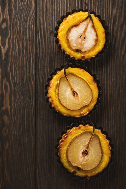 Poires et mini tartes à la crème sur une vieille table en bois brun foncé. Vue de dessus.