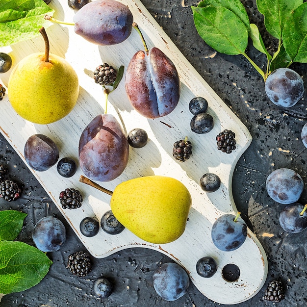 Poires et prunes sur une planche de cuisine blanche