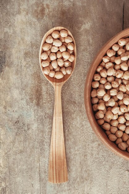 Pois chiches crus dans une assiette en bois et une cuillère sur un fond de bois rustique