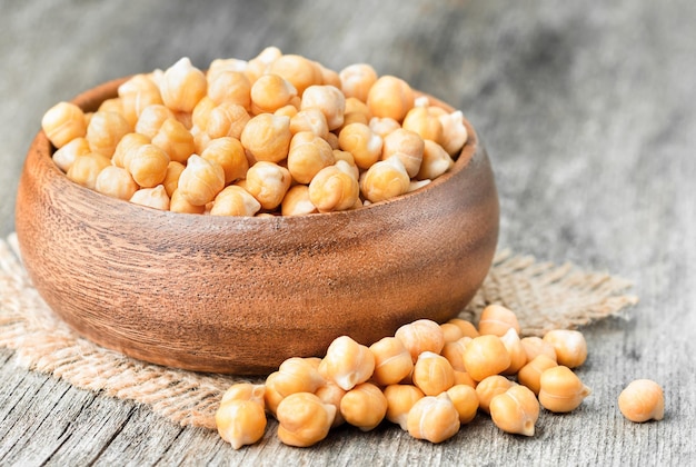 Pois chiches dans une assiette en bois et éparpillés sur la table à proximité